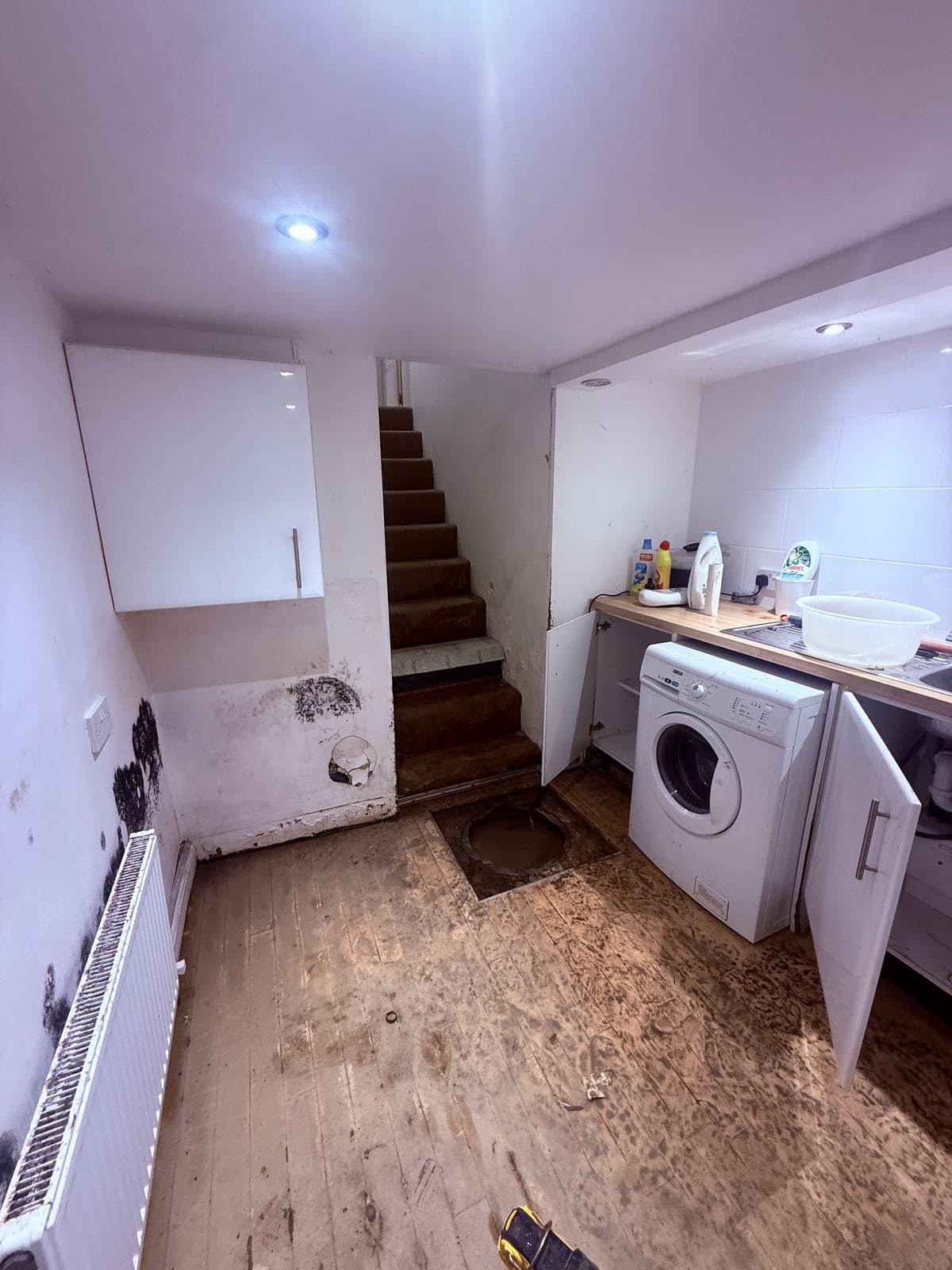 Converted cellar utility room in Leeds with stripped units, a rotten timber floor deck and an open sump chamber