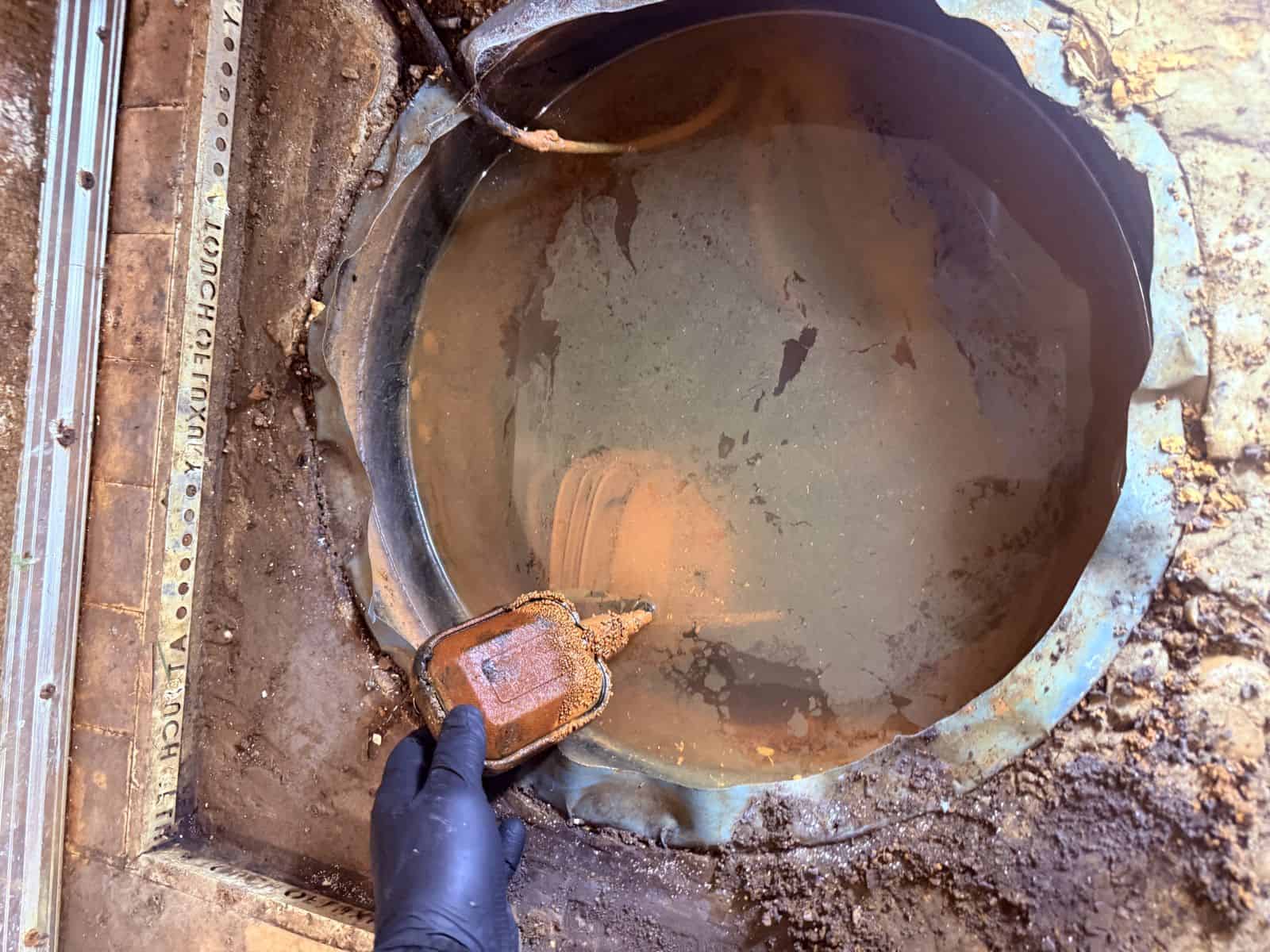 Surveyor lifting a corroded steel cover to reveal silted standing water inside the sump chamber