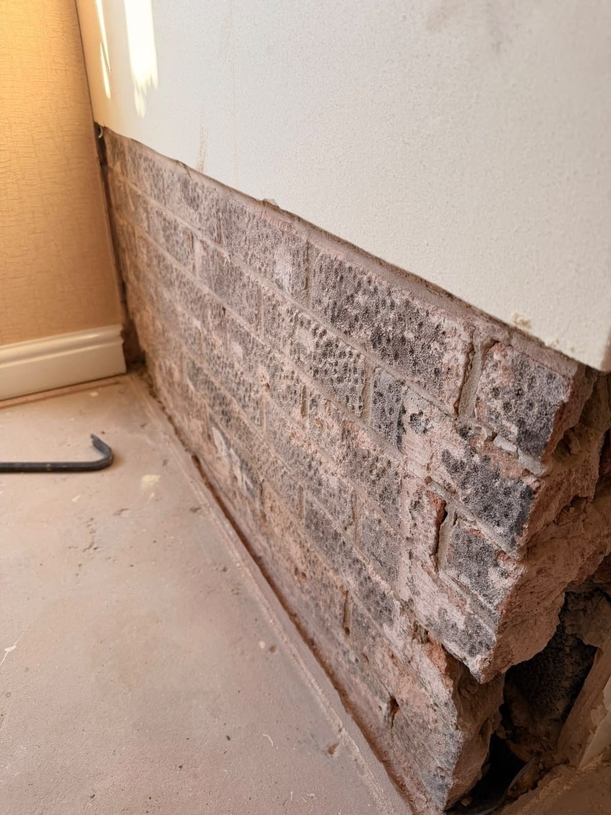 Brickwork exposed after plaster was hacked off along the base of a damp extension wall in Royston
