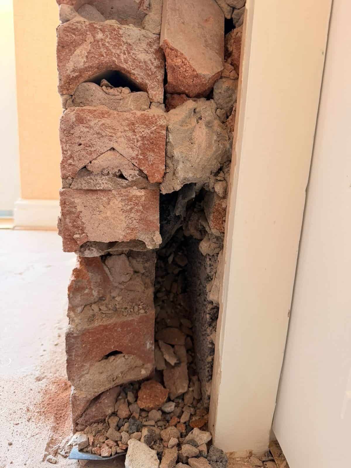 Wall opened up to reveal mortar and brick debris packed in the cavity and bridging over the black damp proof course